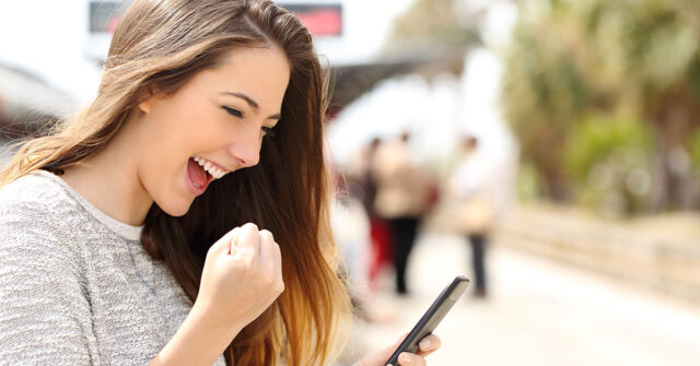 Young woman looking at her phone with a clenched first of excitement after selling her car over the phone.