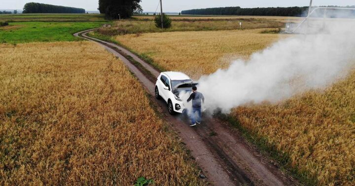 White car on a empty country road with huge plumes of white smoke coming from the overheated engine.