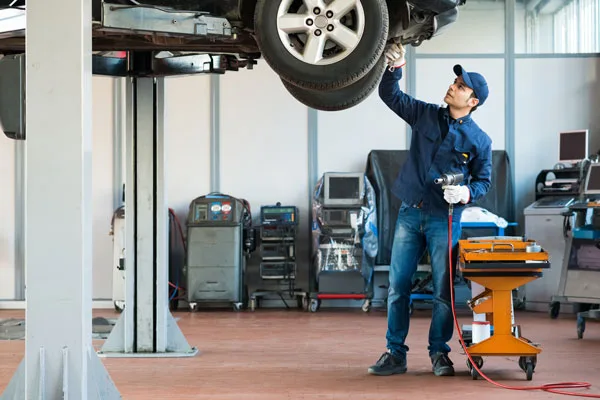 Mechanic looking at the underneath of a motor vehicle on car hoist.