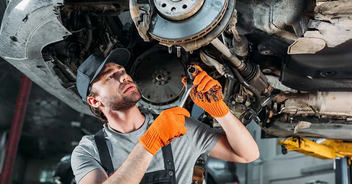 Mechanic holding large ratchet attempting to remove a part while under car on a hoist.