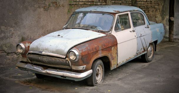 Very old car that has rusted side panels and a flat tyre