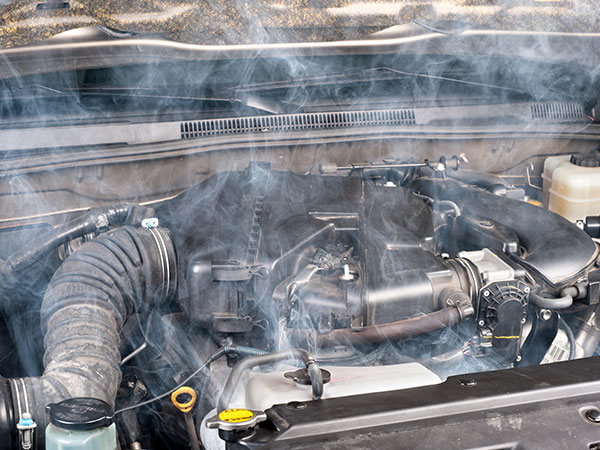 Close up of a hot car engine with smoke coming up off it.