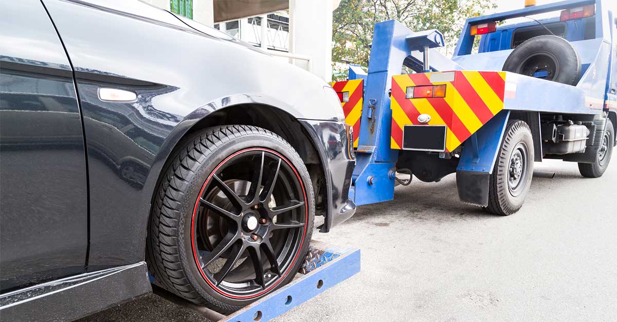 Black car with black wheels being towed away after being sold for scrap.